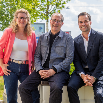 Claudia Braun, Herbert Lang und Daniel Fischer sind zu dritt auf einer Bank. Im Hintergrund sieht man Bäume, Hecke und ein Gebäude.