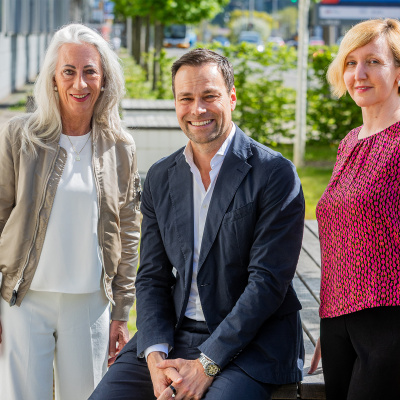 Claudia Romahn, Daniel Fischer und Susanne Stoeck auf einer Bank vor Hecken und Weg.