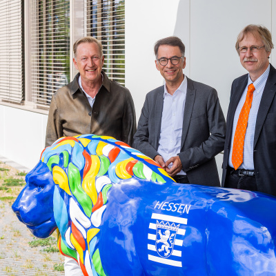 Folke Mühlhölzer, Christian Heinz und Alexander Bracht stehen vor einer großen, blauen Löwen-Statue vor einem Gebäude.