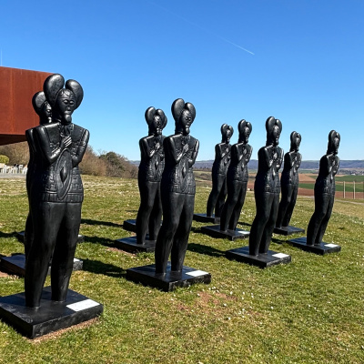 Mehrere Keltenfürstenskulpturen am Glauberg auf einer grünen Wiese. Das Museum Keltenwelt am Glauberg im Hintergrund leicht sichtbar.