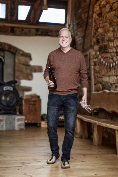 André Hülsbömer mit einer Flasche Wein und einem Glas in der Hand.