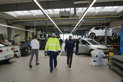 Mehrere Männer laufen durch eine Autowerkstatt.