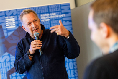 Folke Mühlhölzer, Vorsitzender der Geschäftsführung der HA Hessen Agentur GmbH hält ein Mikrofon und spricht zum Publikum.