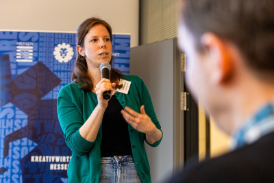 Daniela Hartmann hält ein Mikro und spricht zum Thema Fördermöglichkeiten für Gründer der Games-Branche zum Publikum.