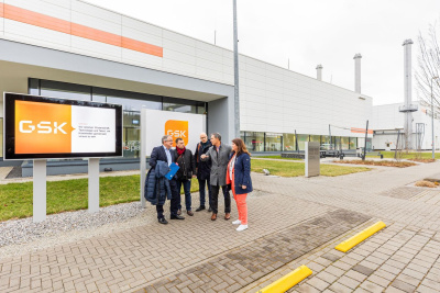 Fünf Personen stehen vor einem Industrie-Gebäude. Auf einem Schild neben den Personen steht GSK.