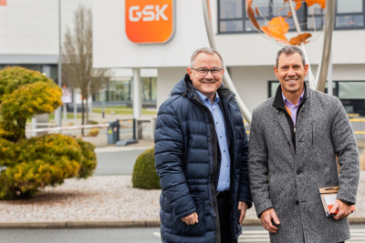 Zwei Männer stehen vor einem Gebäude und lächeln in die Kamera. Hinter ihnen steht eine Skulptur mit einem Globus.