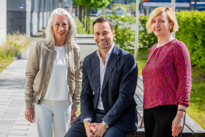 Claudia Romahn, Daniel Fischer und Susanne Stoeck auf einer Bank vor Hecken und Weg.