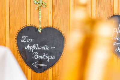 Schild in Herzform mit der Aufschrift "zur Apfelwein Boutique" vor einer holzgetäfelten Wand