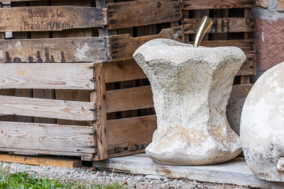 Große Steine in Apfelform gemeißelt vor alten Holzkisten.