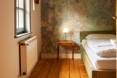 Ein Hotelzimmer im Auenlandhof von innen. Man sieht ein Bett mit Nachttisch.
