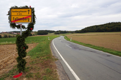 Landstrasse durch Felder mit Ortsschild auf der linken Seite