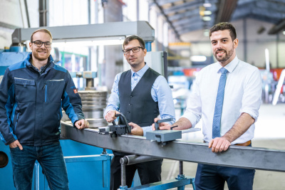 Drei Männer stehen in einer Fabrik vor einem mobilen Handmessgerät.