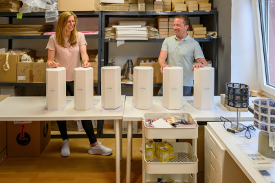 zwei Menschen verpacken Lampen in zylindrische Kartons.