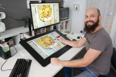 Illustrator Raimund Frey sitzt an seinem Schreibtisch und zeichnet den Hessen-Löwen.