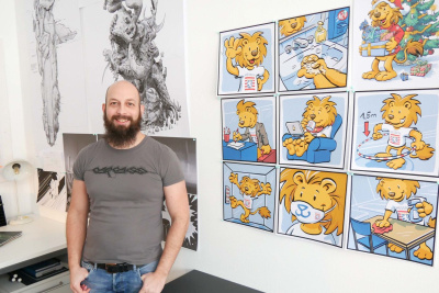 Der Illustrator Raimund Frey steht vor den Zeichnungen des Hessen-Löwen.