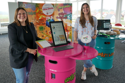 Sarah Neumeyer und Anke Volkemer stehen an einem pinken Tisch mit Tablets.