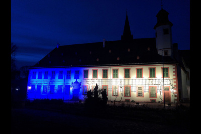 Man sieht das Kloster Seligenstadt im Dunkeln, angestrahlt von Schweinwerfern in den Farben Blau und Gelb.