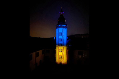 Man sieht den Pfeiferturm von Schloss Weilburg im Dunkeln, angestrahlt von Scheinwerfern in den Farben Blau und Gelb.