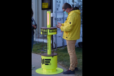 Ein Mann steht an einer mobilen Handyladestation im Freien und schaut auf sein Smartphone.