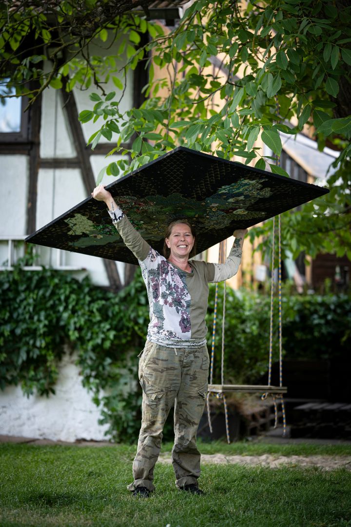 Christine Zimmer-Spangenberg trägt ihr Bild durch den Garten. Im Hintergrund ist eine Schaukel.