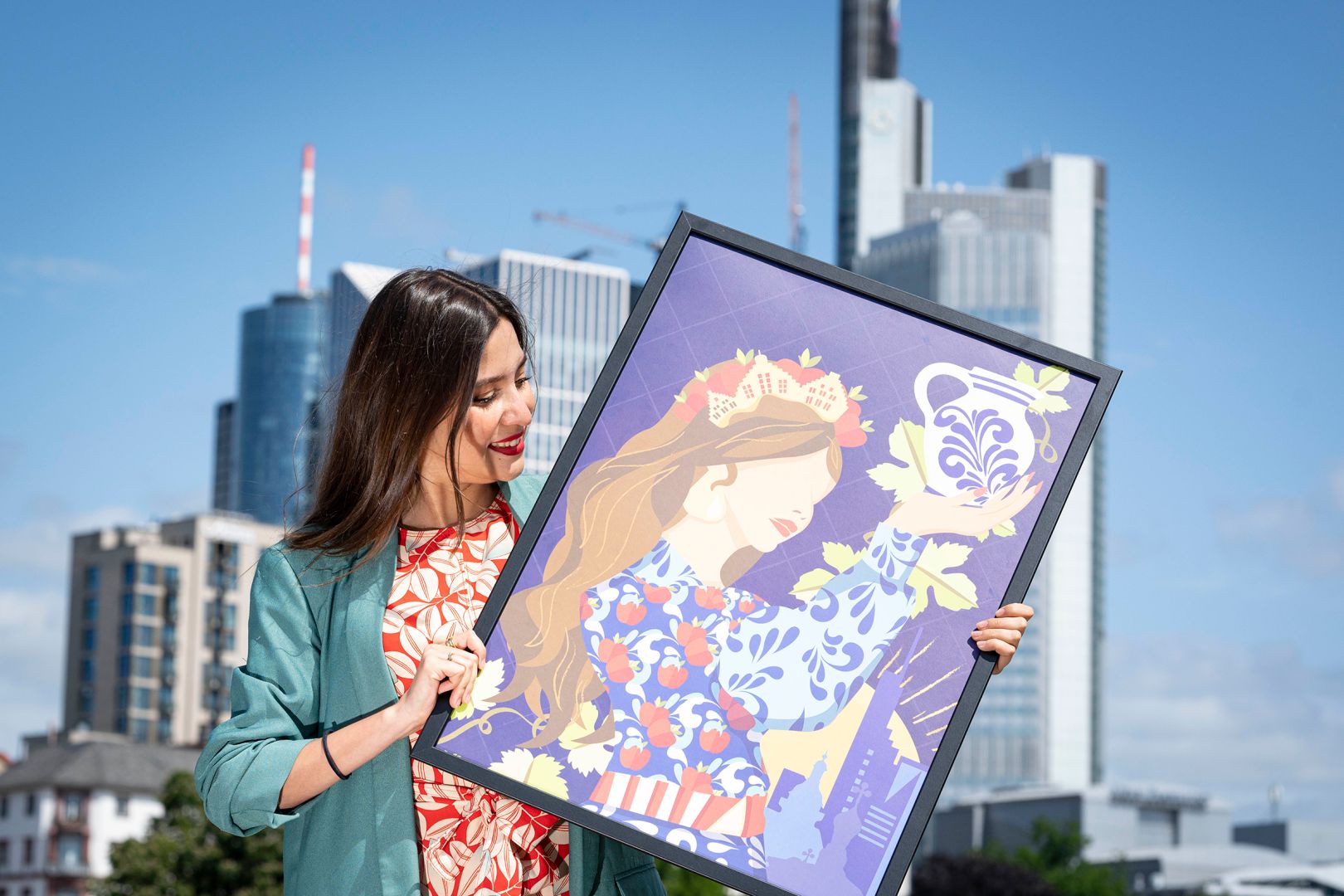Ana Paola Paniagua hält ihr Bild in der Hand, im Hintergrund ist die Frankfurter Skyline zu sehen.